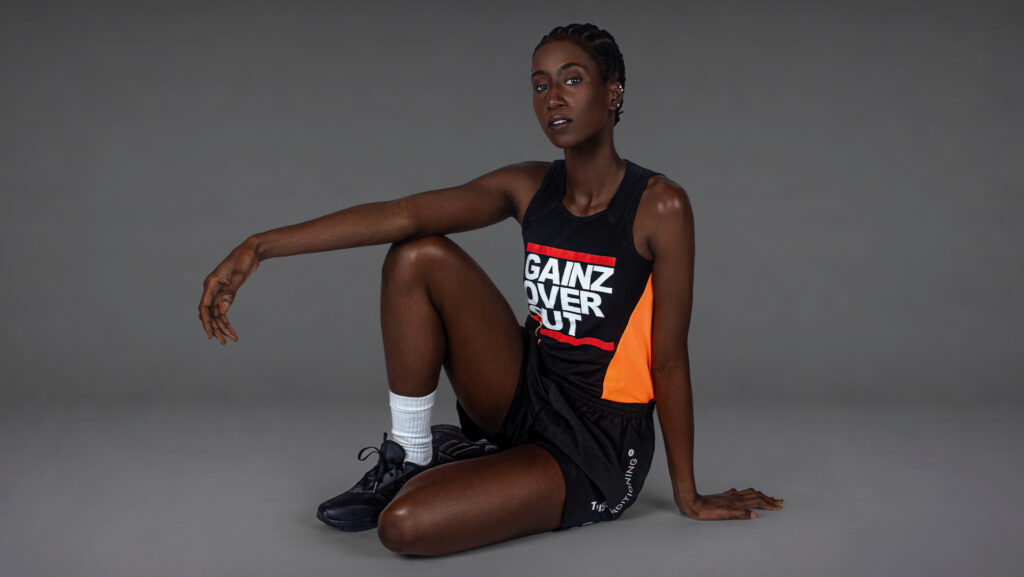 Gigi seated on the studio floor in black and orange activewear for the Strength in Motion editorial