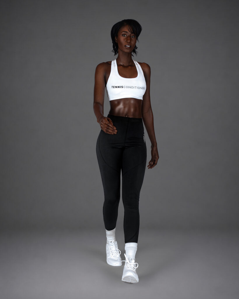 Gigi stepping forward in a white sports bra and black leggings during an athletic fashion studio shoot