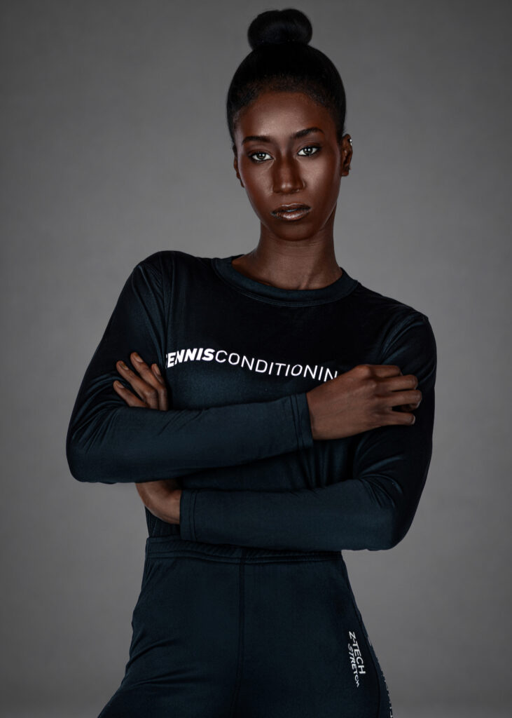 Portrait of Gigi with folded arms wearing black long-sleeve activewear against a gray studio background