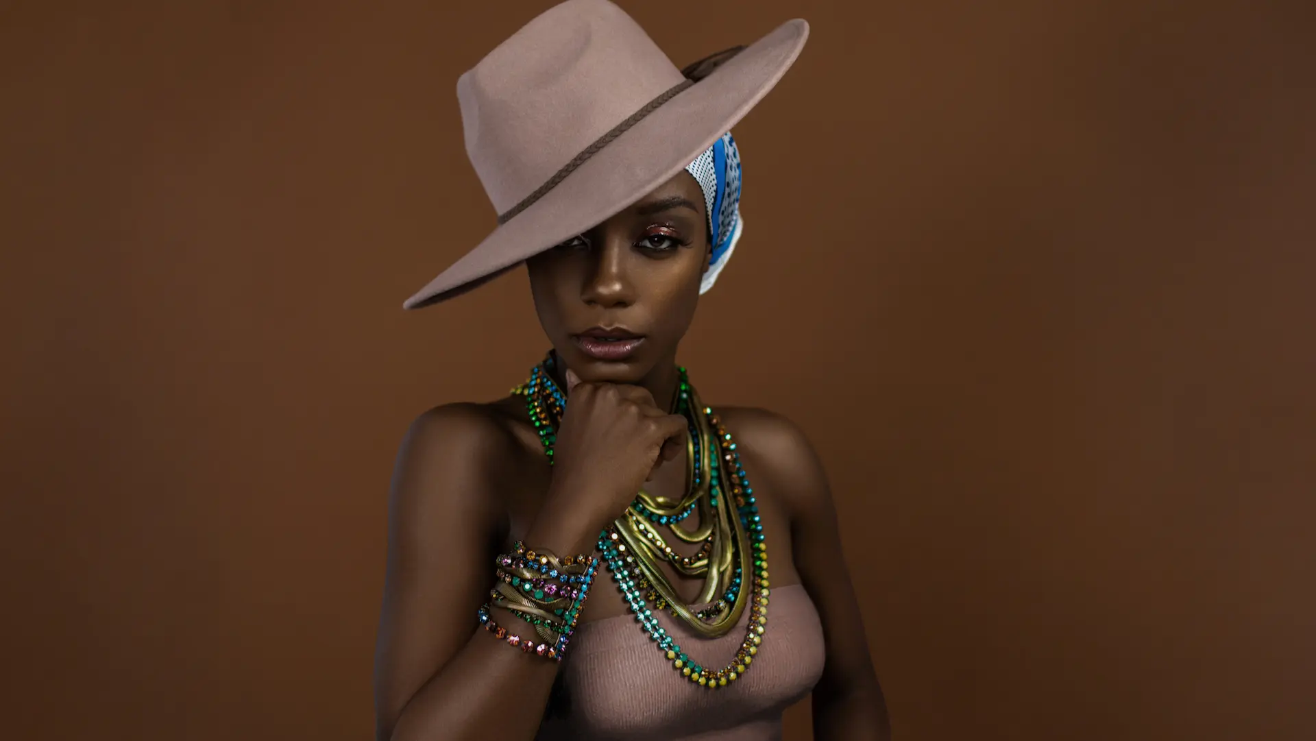 Black woman in a grey hat with luminous makeup and colorful statement jewelry