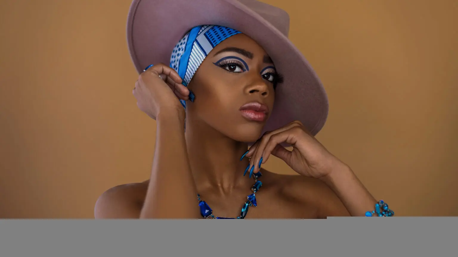 Black model wearing a blue-and-white headscarf, grey hat and blue jewelry
