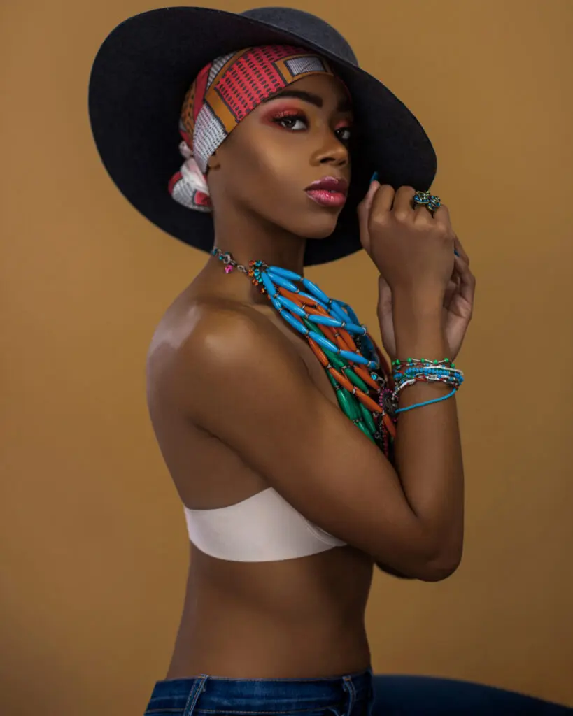 Black woman wearing a red-and-white headscarf, grey hat and statement jewelry