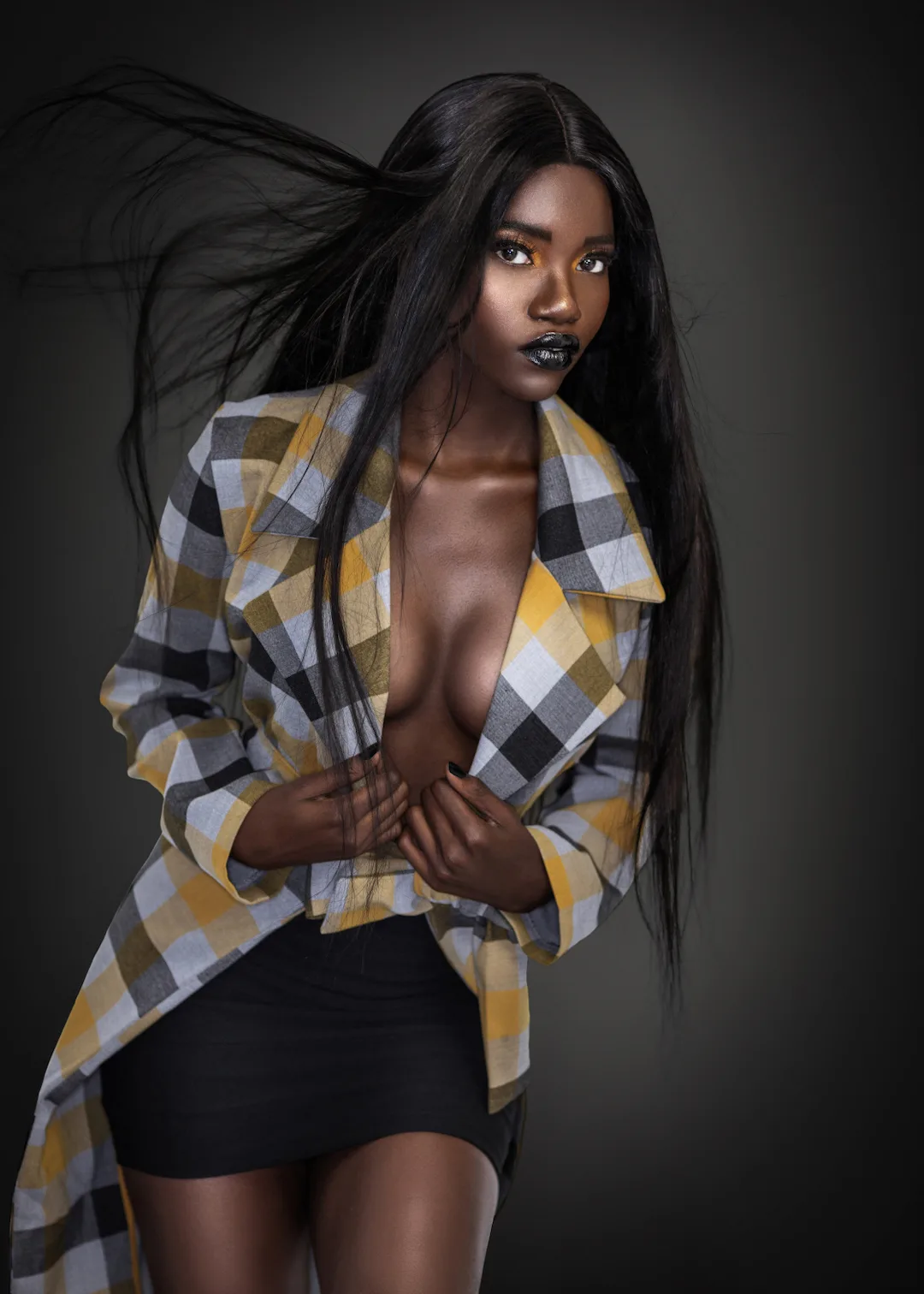 Studio portrait with long hair, deep lipstick and a colorful coat against a dark background.