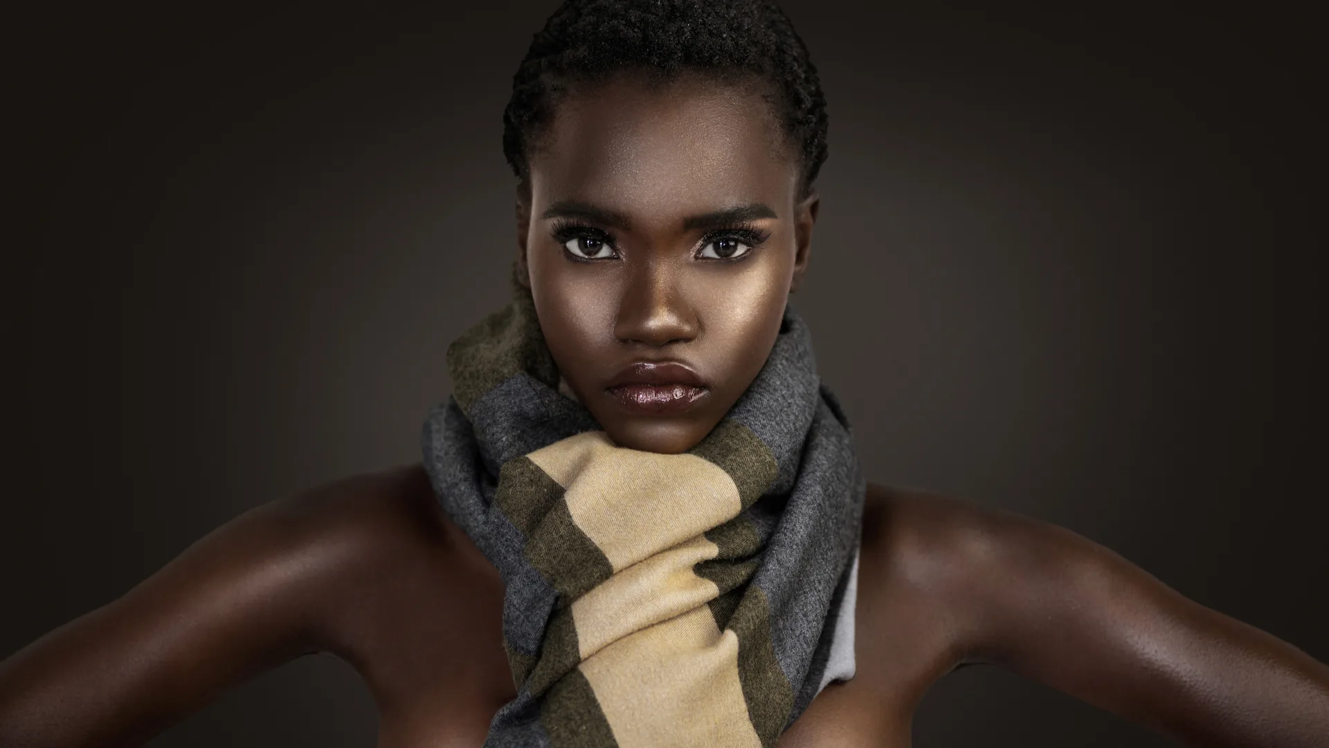 Studio beauty portrait wrapped in a colorful scarf against a dark background.