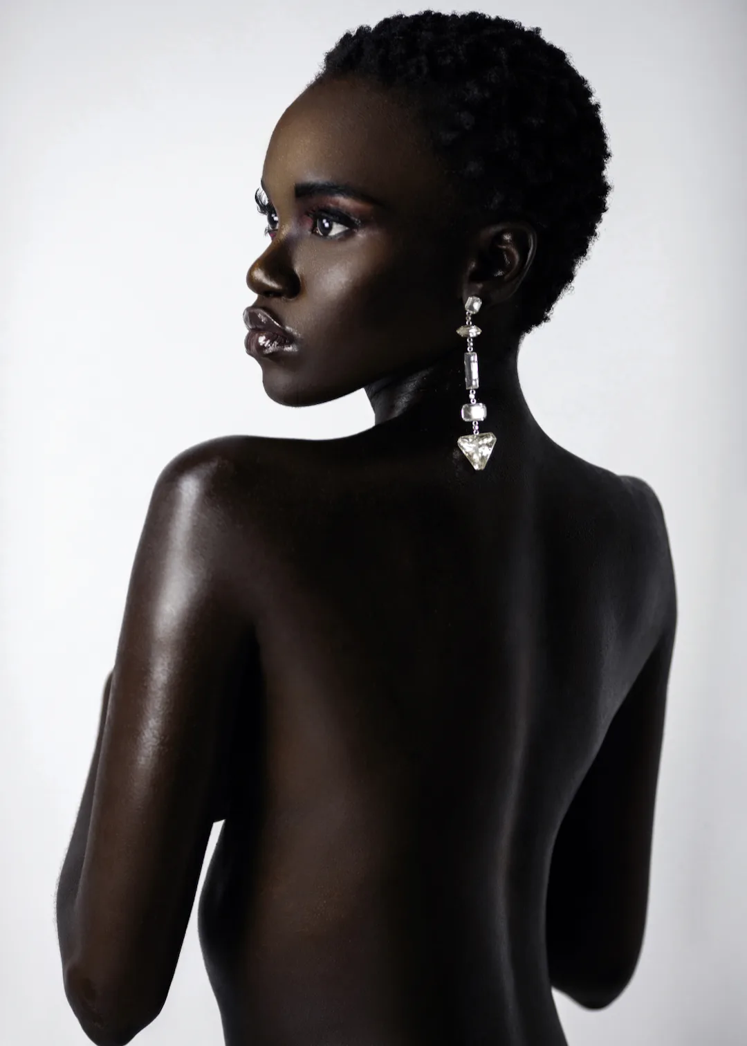 Close-up studio beauty portrait with short hair and diamond earrings against a bright background.