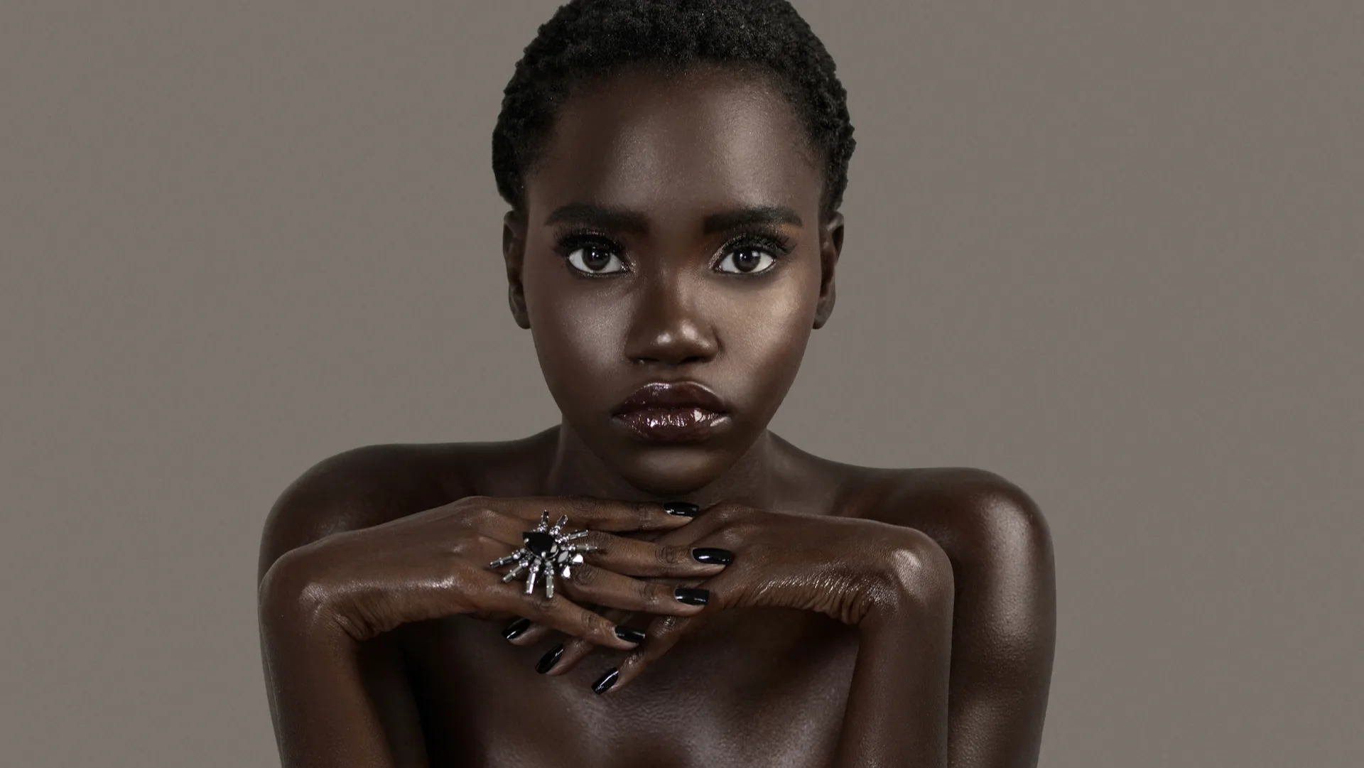 Studio beauty portrait with hands framing the face, a black manicure and silver jewelry.