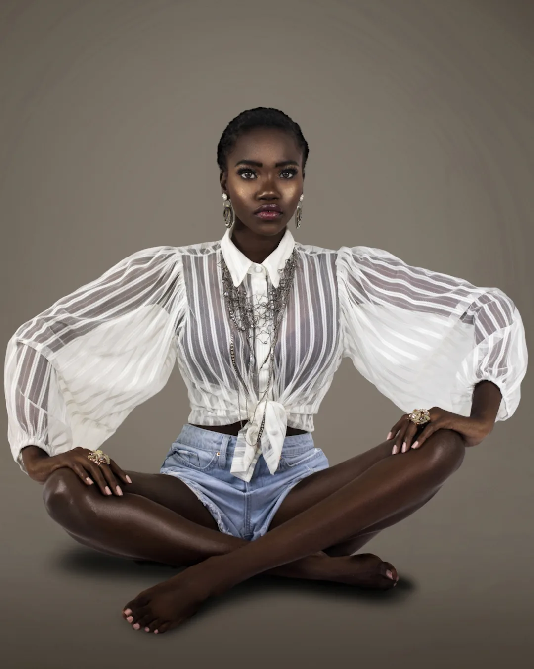 Seated studio portrait in a sheer white blouse, denim and silver jewelry.