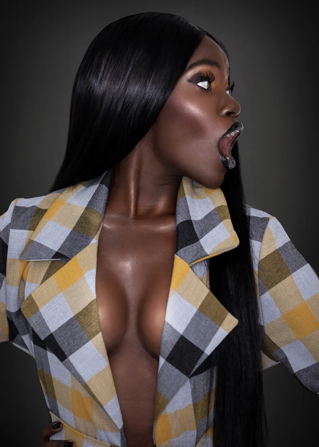 Serene studio beauty portrait with long hair and deep-toned makeup against a dark background.