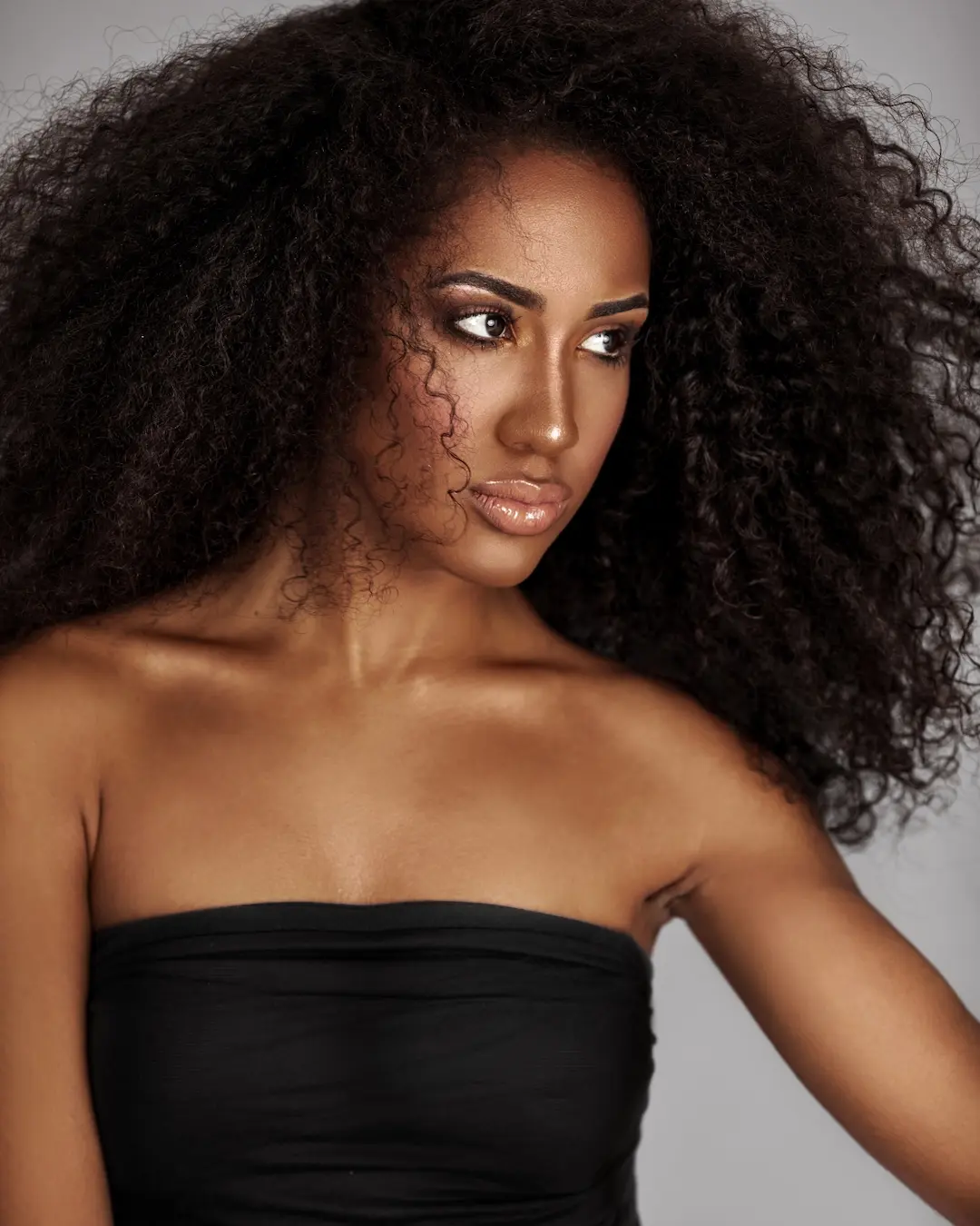Close-up beauty portrait of Willina Rodriguez wearing a black wrap top with defined natural curls