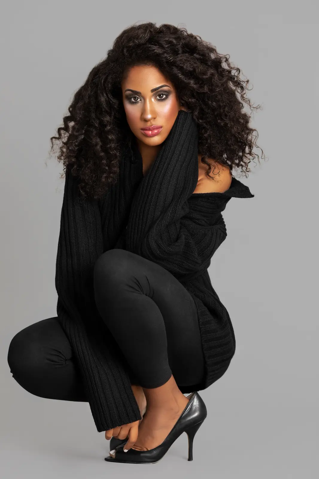 Full-length studio portrait of a curly-haired model in a black wool sweater and heels
