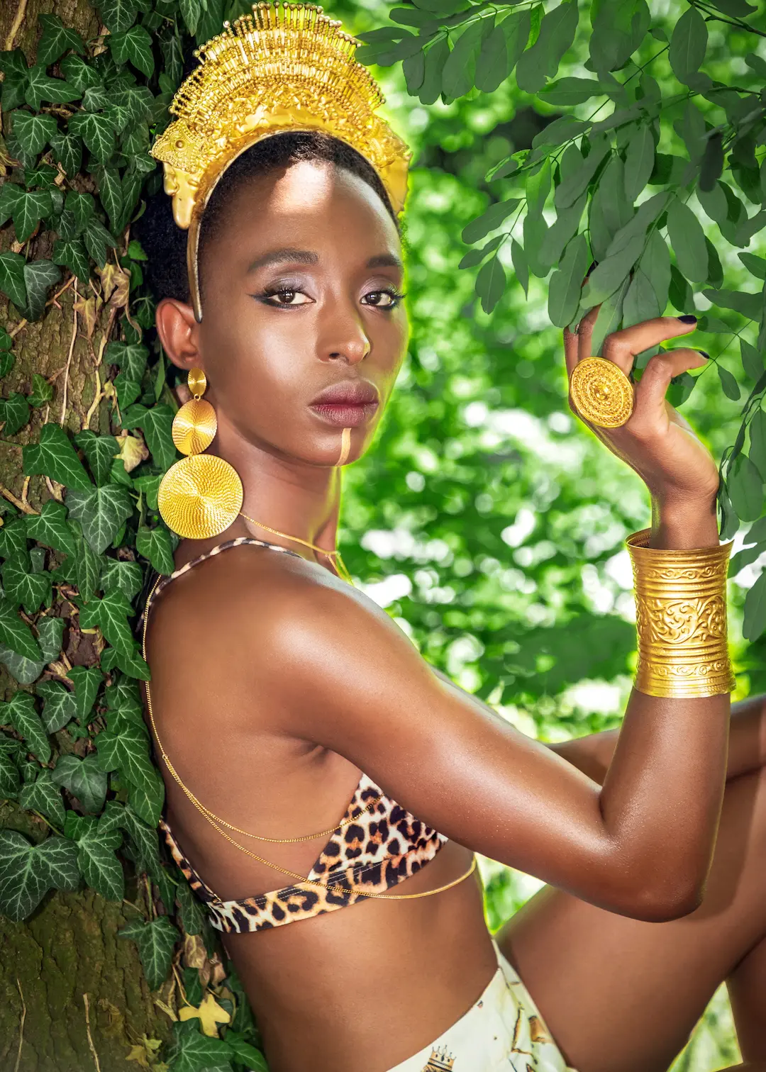 Woman wearing a sculptural gold headpiece and jewelry in a green outdoor setting