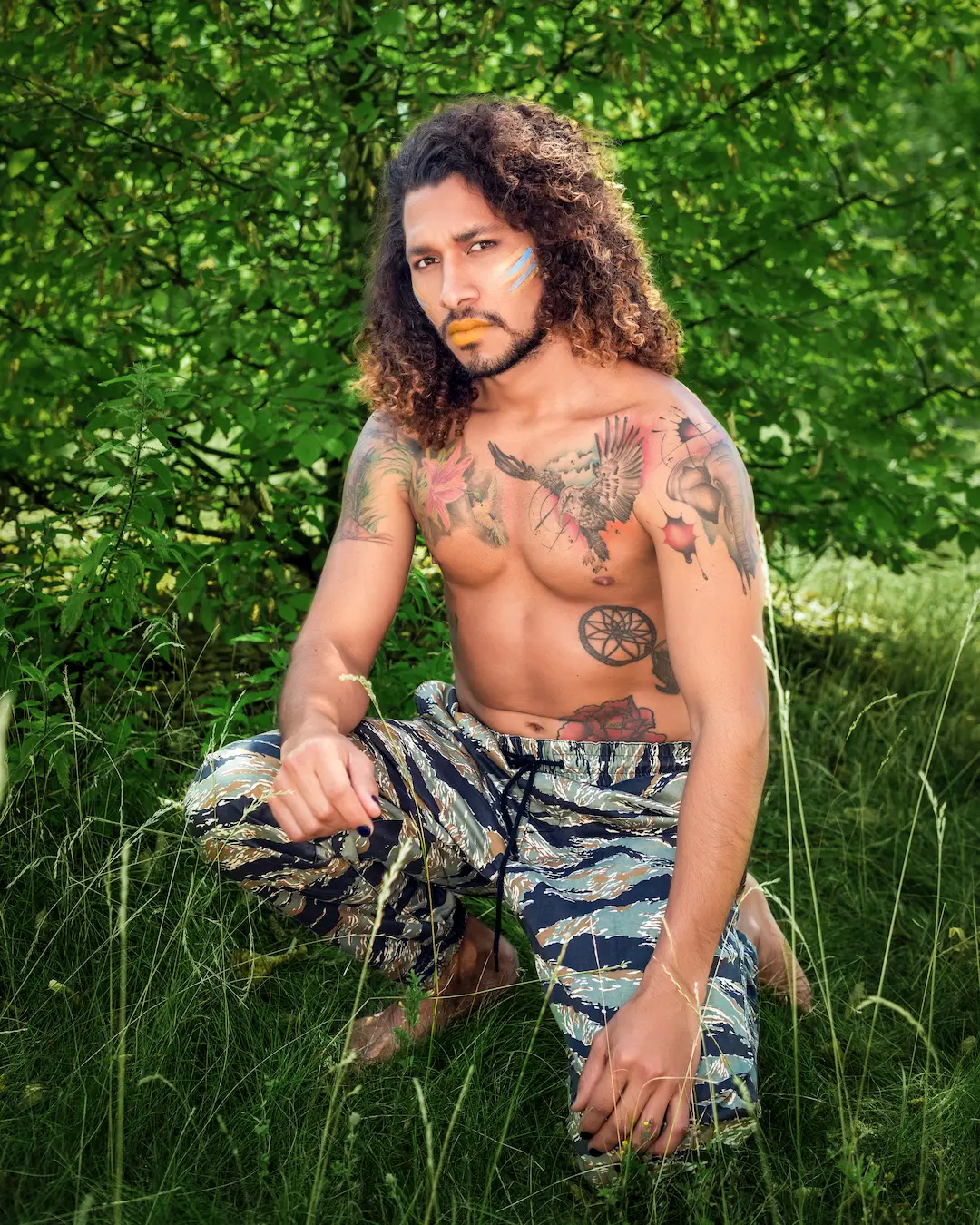 Man seated in tall grass wearing layered jewelry and patterned styling