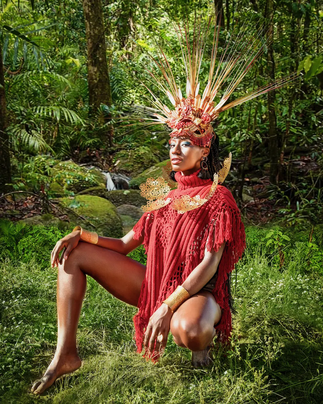 Woman in a red dress and sculptural headpiece seated in a forest