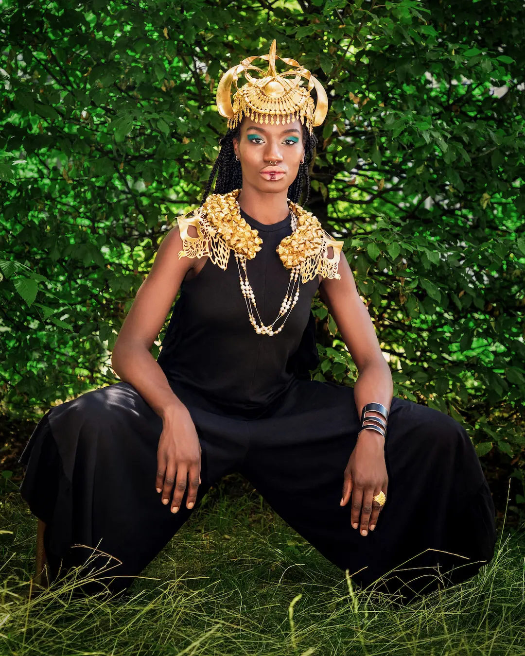 Woman seated in black clothing and ornate gold jewelry outdoors
