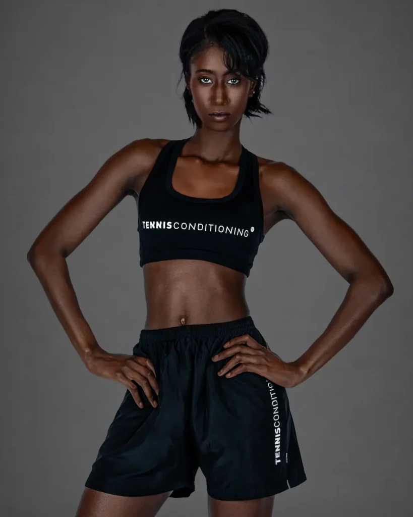 Gigi wearing a black sports bra and black athletic shorts in a confident studio portrait