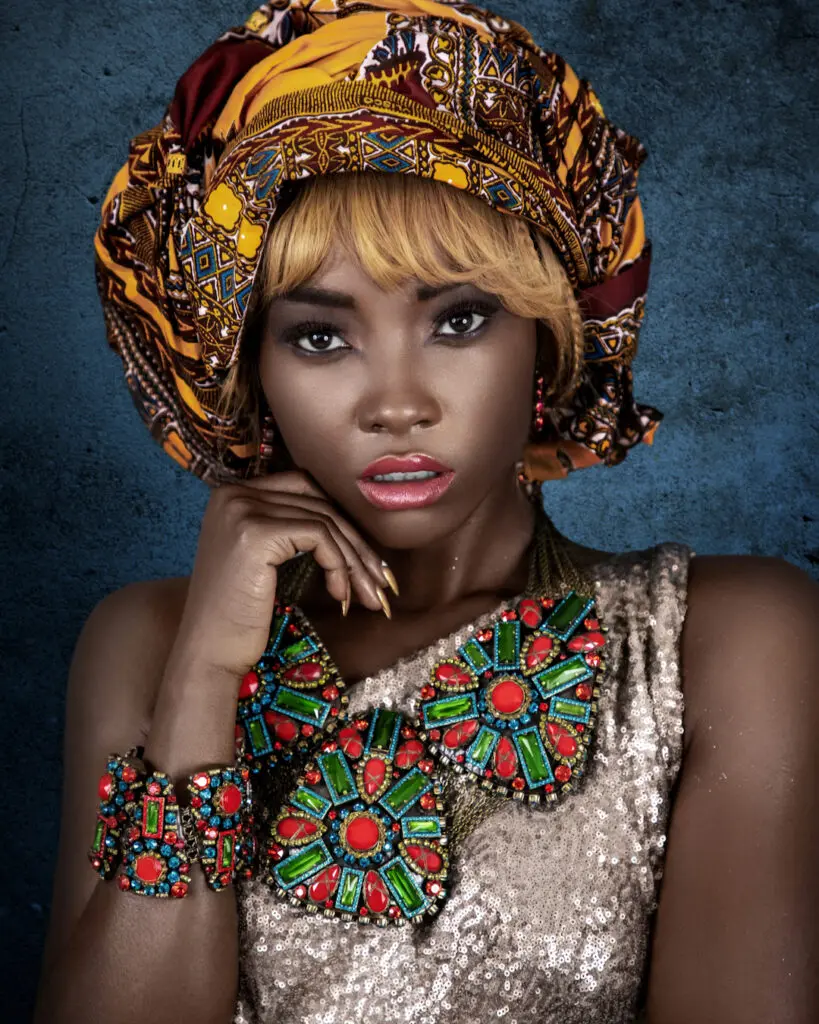 Black woman in a gold dress, orange patterned headscarf and colorful jewelry