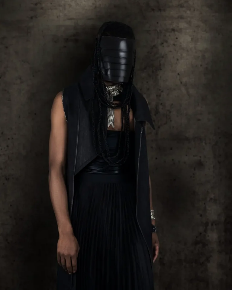Black woman in a black avant-garde dress and silver jewelry against a dark studio background