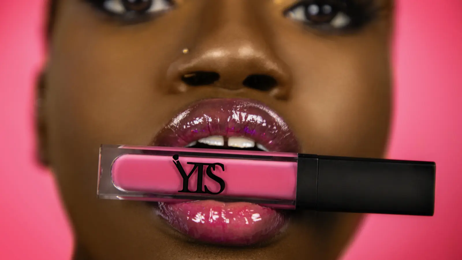 Close-up of a model holding pink lip gloss against glossy pink lips
