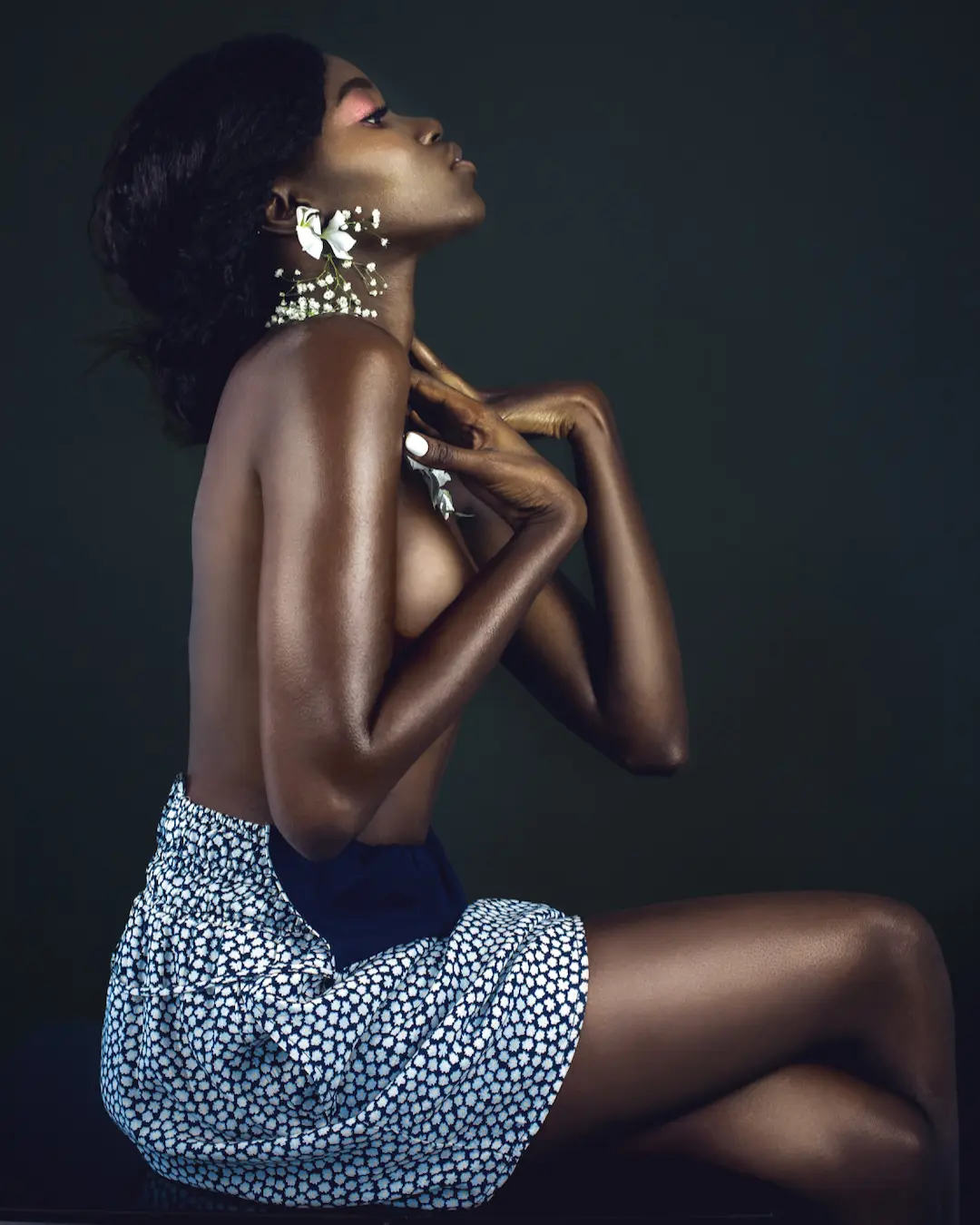 Profile portrait of a Black model wearing white floral earrings and body adornment