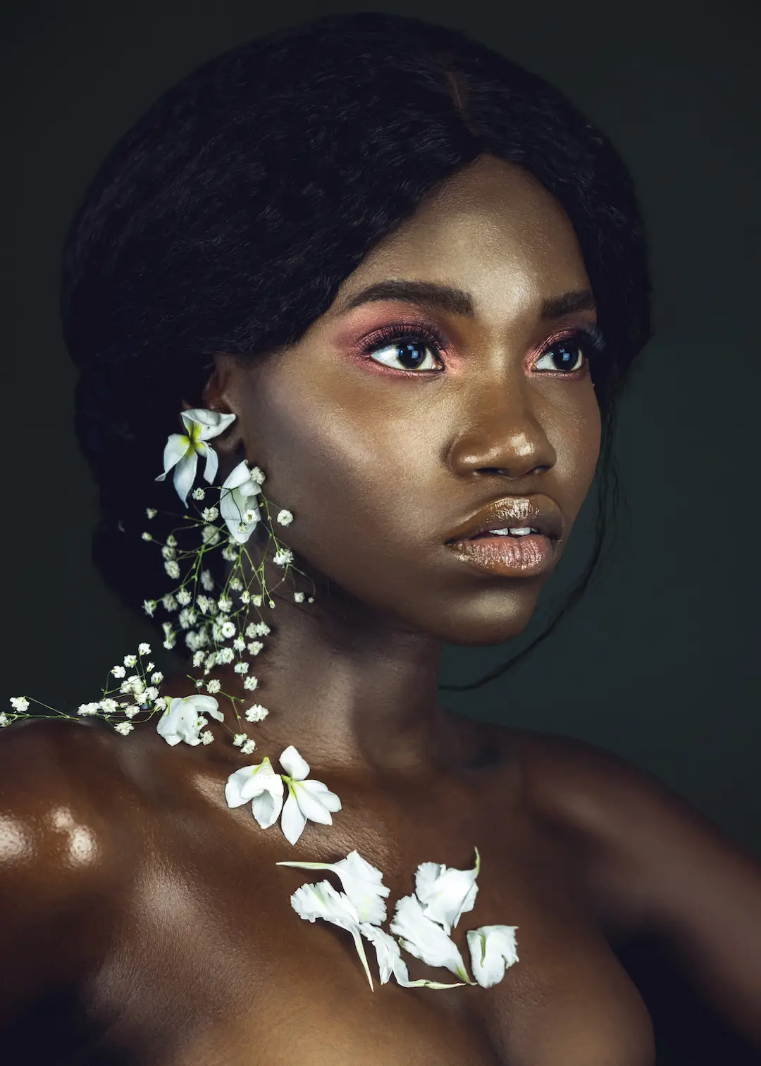 Black model with long natural curls and white flowers in a studio beauty portrait
