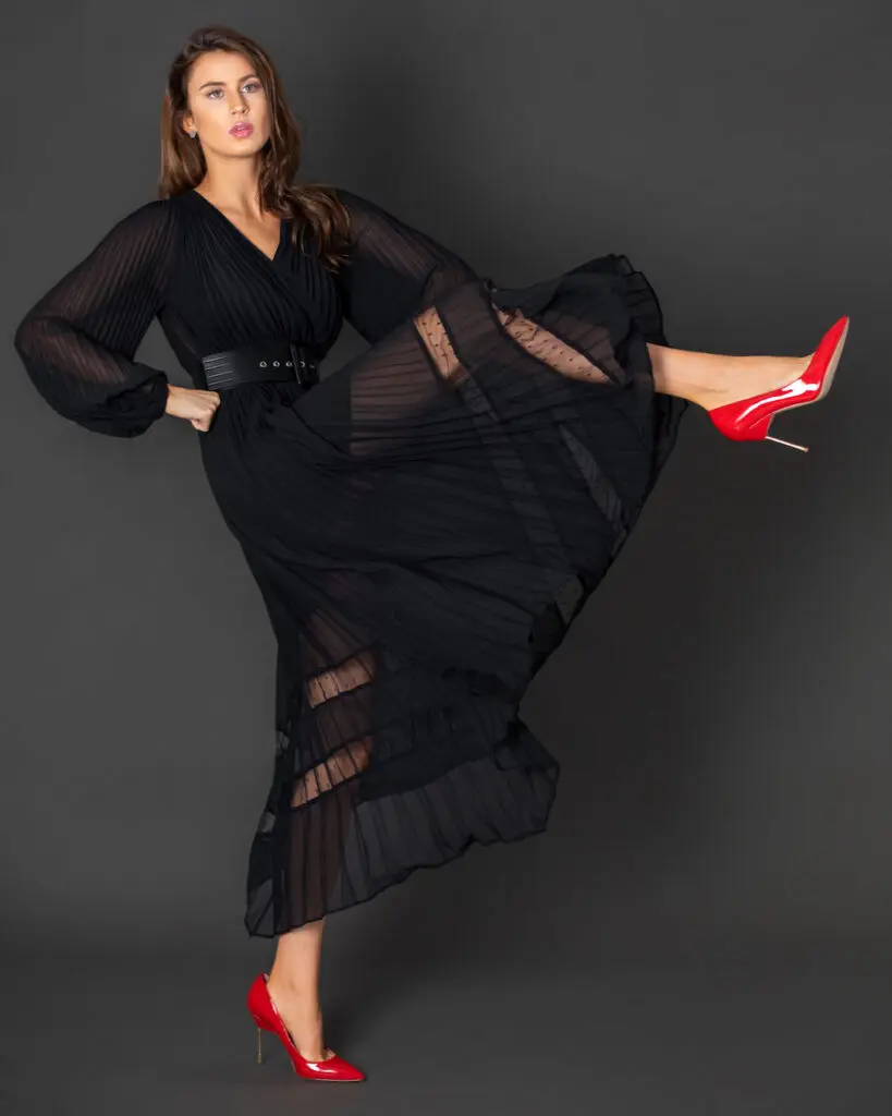 Rebecca wearing a belted black dress and red heels in a studio editorial