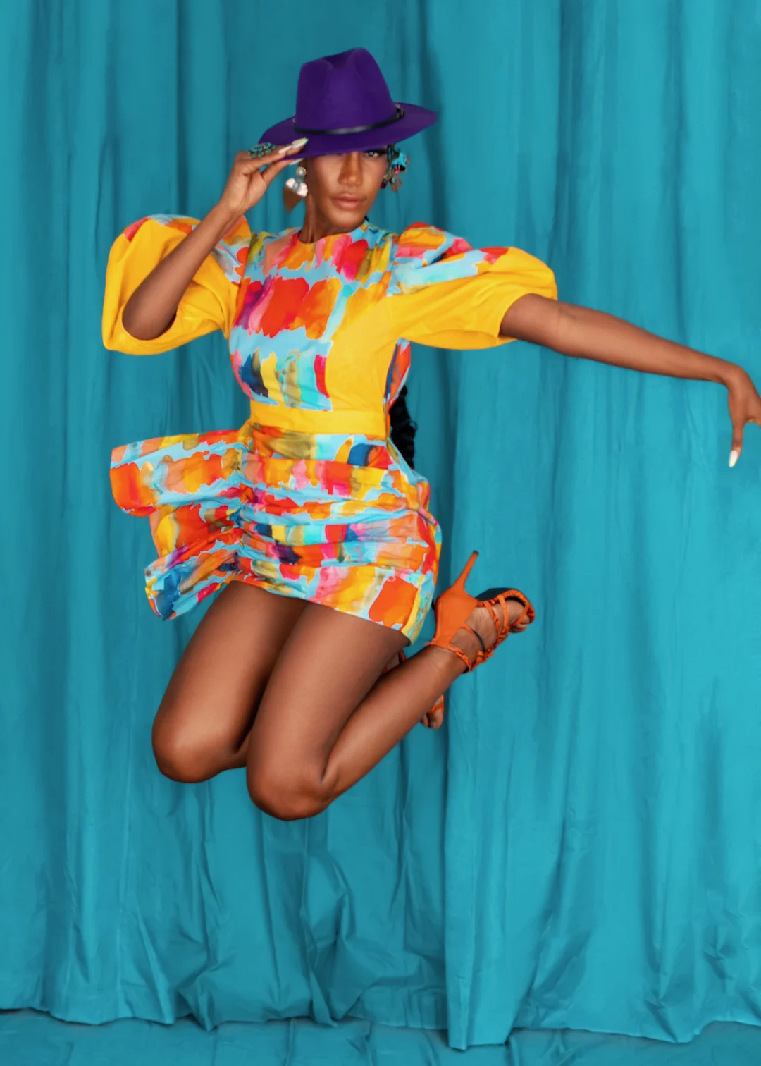 Claudine wears a colorful short dress with a sculptural purple hat in The Reemerging editorial.