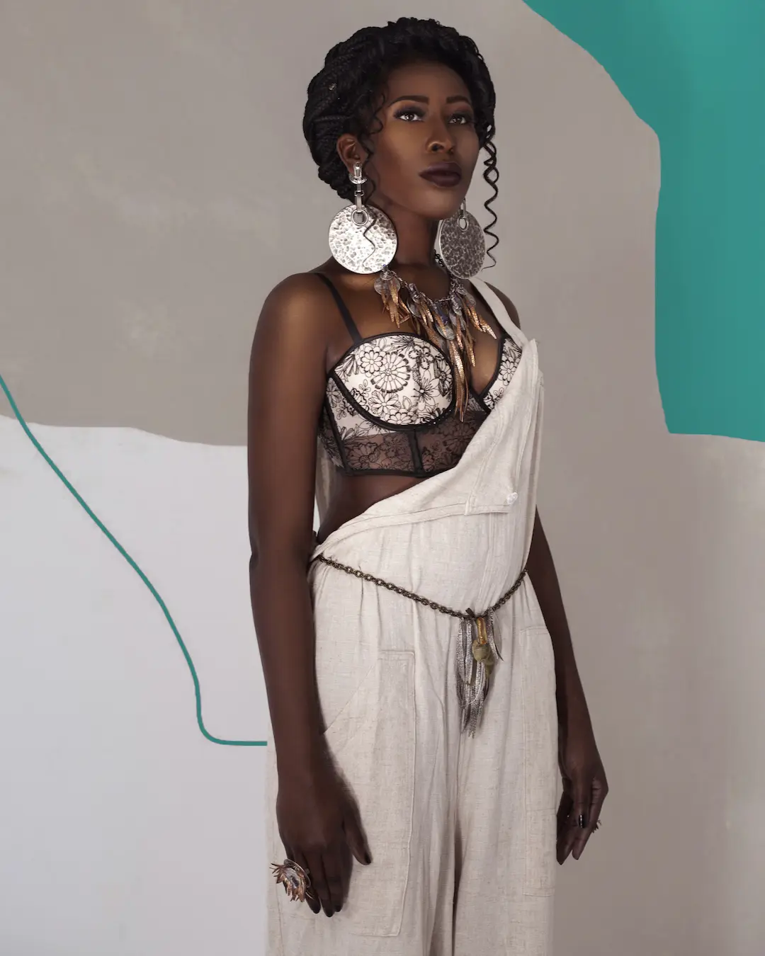 Black woman with natural curls wearing a colorful outfit and silver jewelry in a white studio.