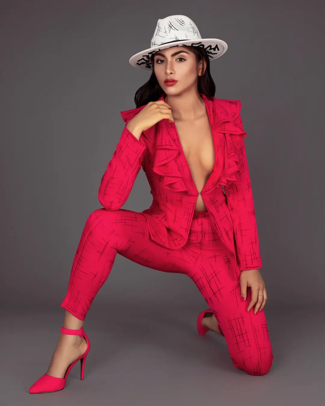Model wearing a red tailored suit and white hat in a studio fashion portrait