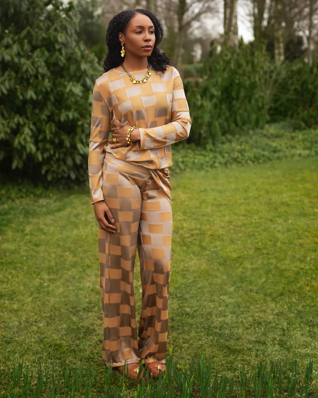 Woman in a golden checkered outfit photographed in a garden