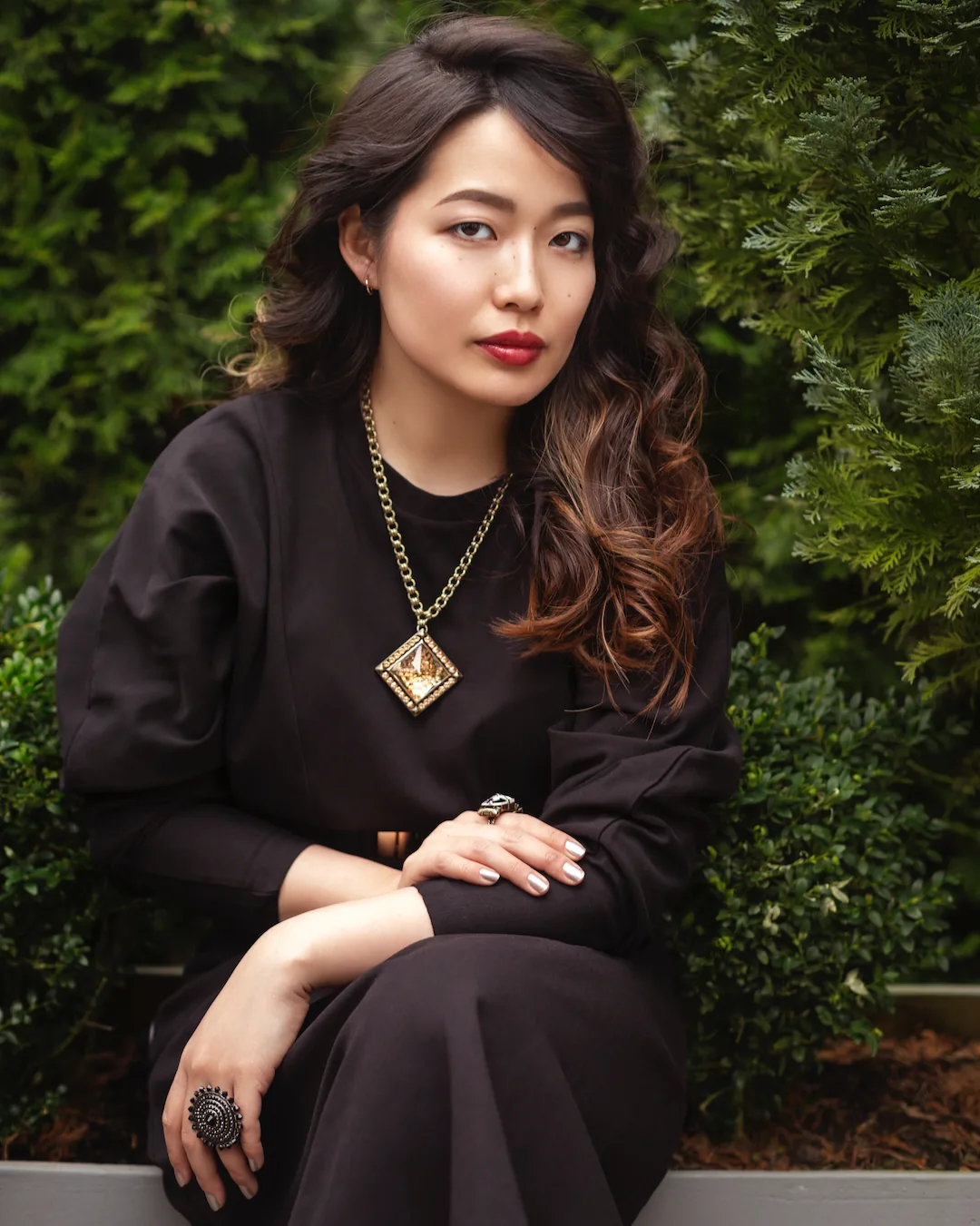 Woman in a black dress standing before green hedges