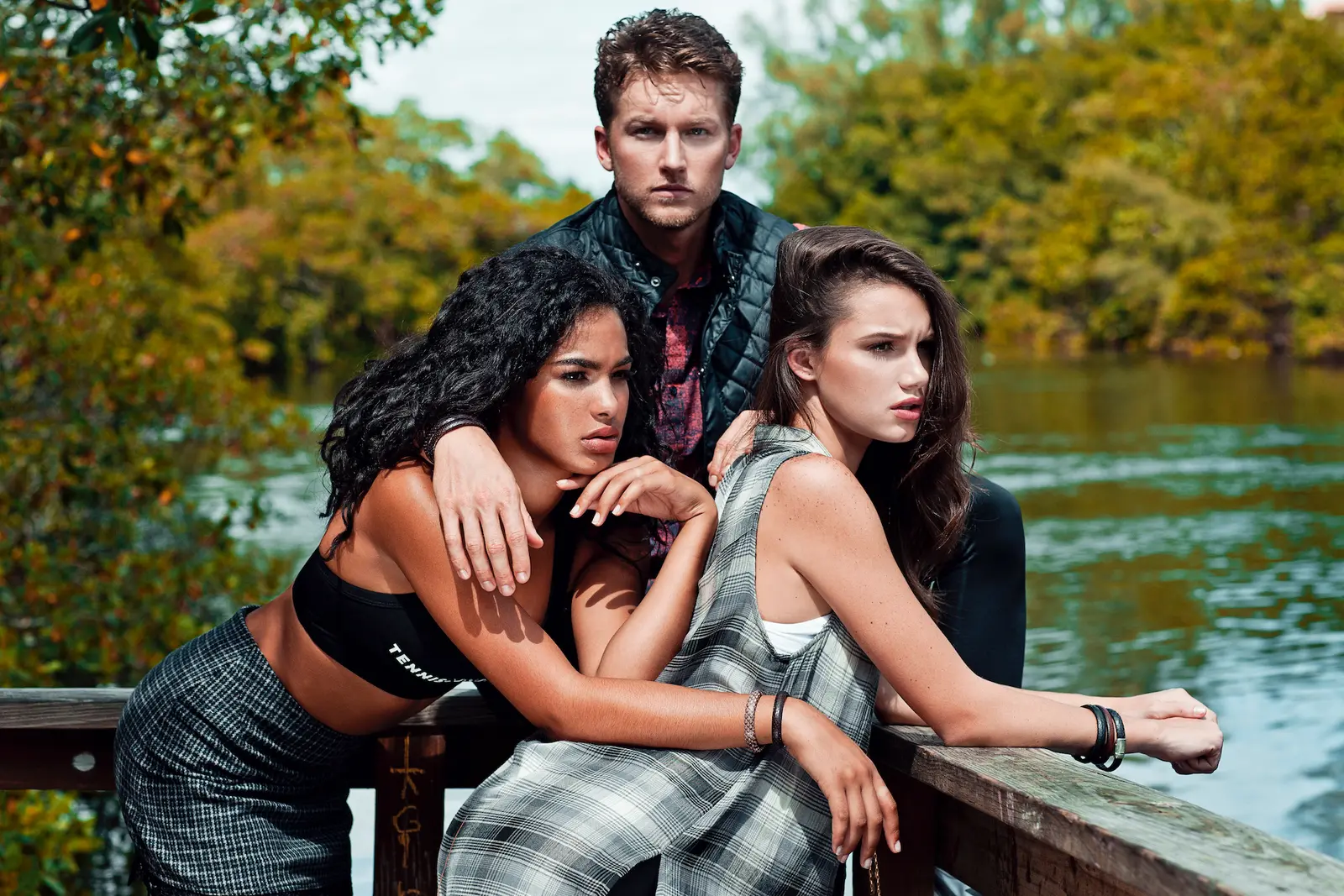 Three models in urban fashion pose together beside a lake in a Miami park.