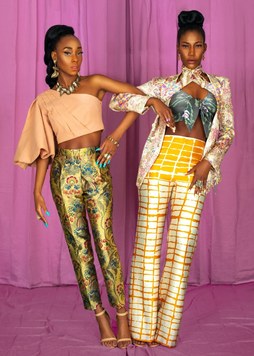 Vanessa and Claudine pose together in colorful fashion looks against a pink studio backdrop.