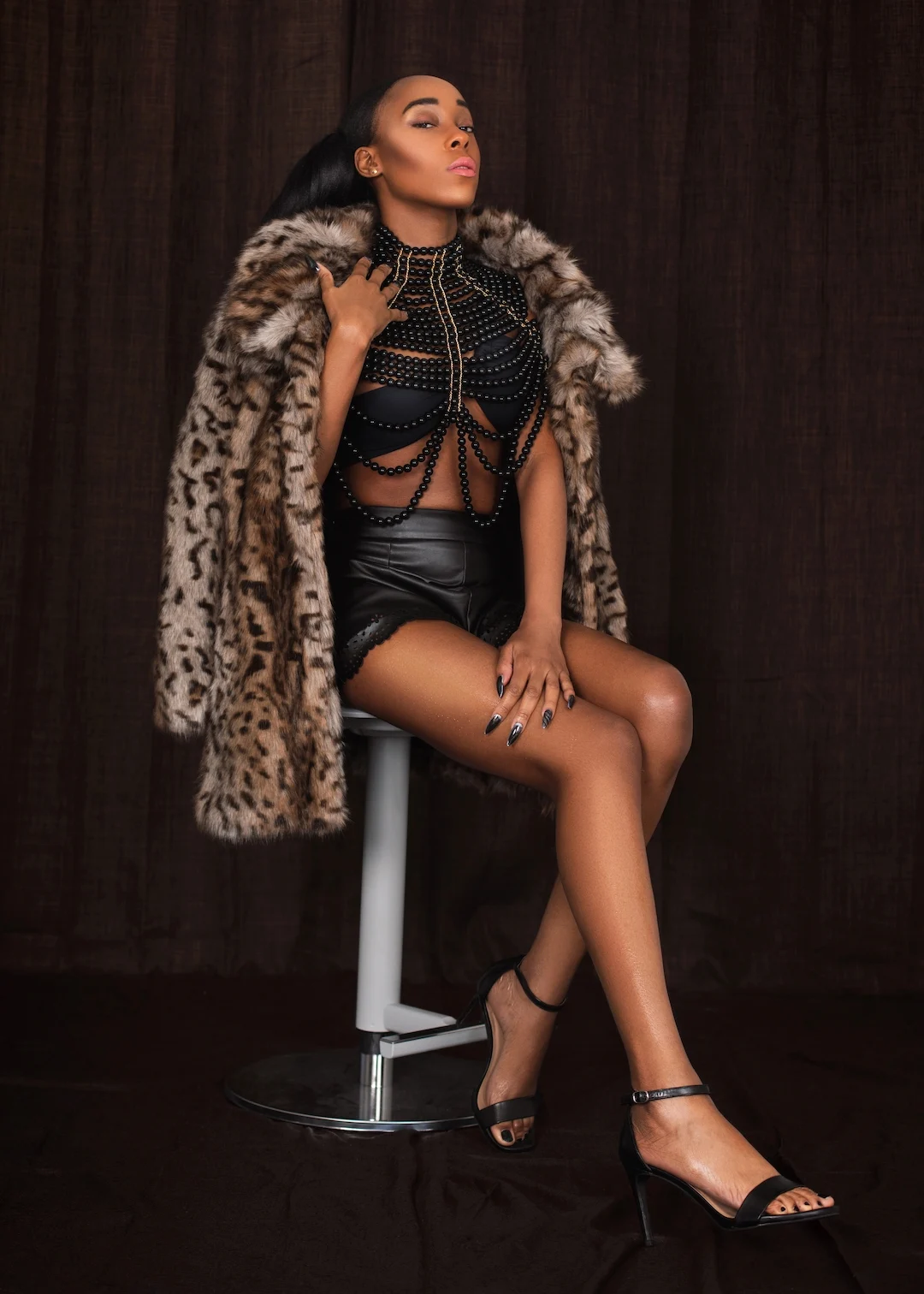 Vanessa wears black leather shorts and a leopard-print faux-fur coat in The Reemerging fashion editorial.