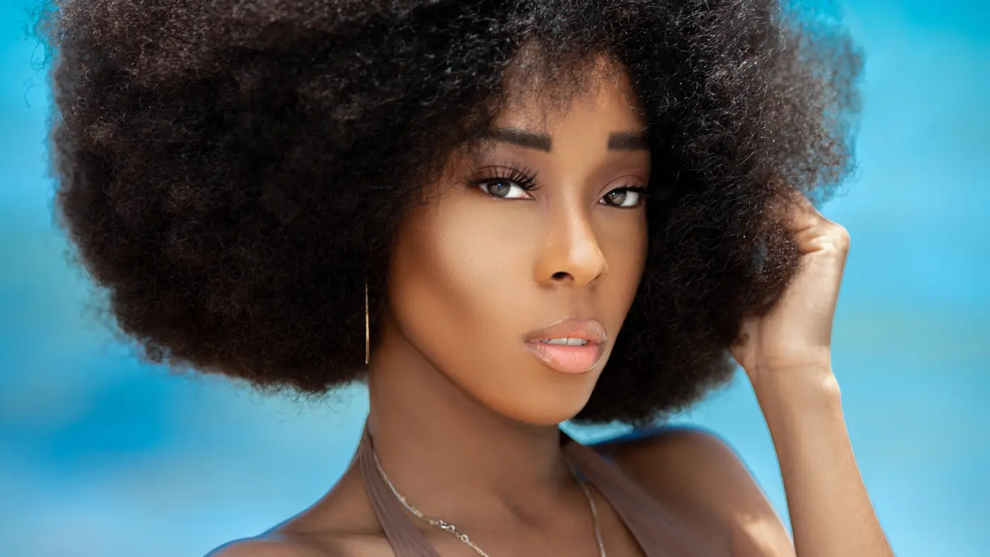 Black model with a voluminous Afro posing in brown swimwear on a Miami beach