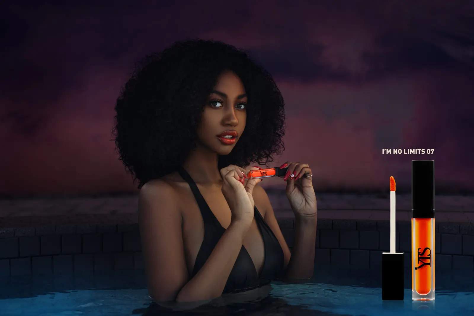Model holding orange lipstick in a dark poolside beauty campaign image