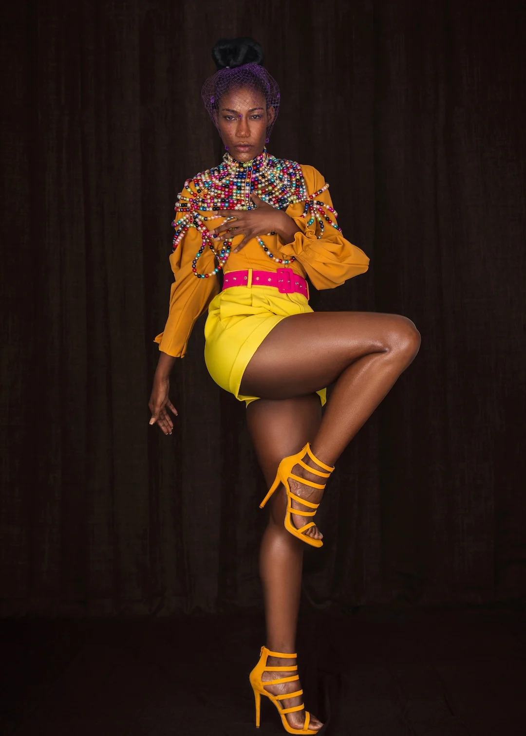 Vanessa wears yellow shorts and an orange blouse with colorful pearl details and a purple veil.