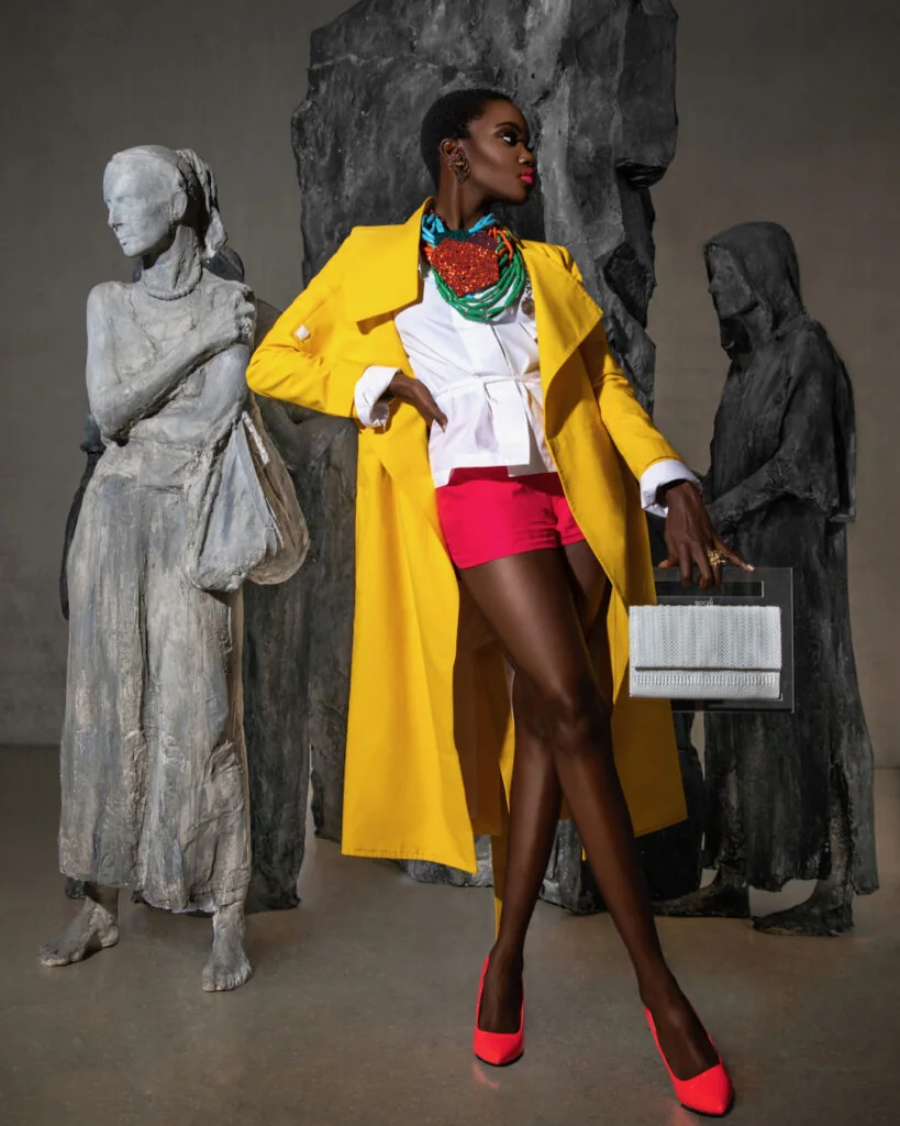 Model in a yellow coat and pink shorts beside sculptures at Pérez Art Museum Miami