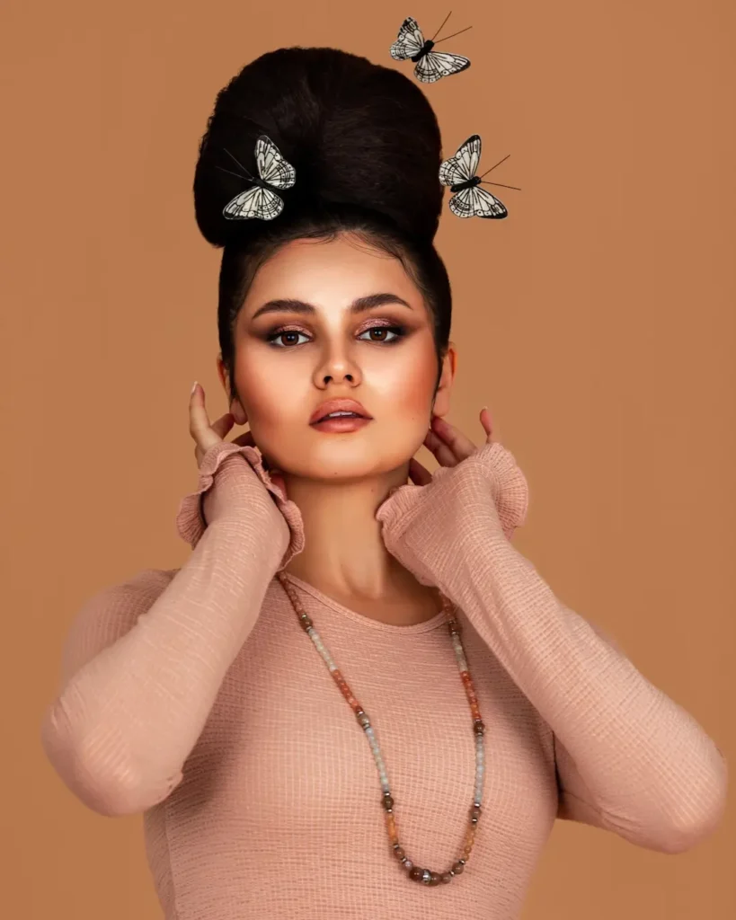 Mariana in a soft pink knit look with butterfly details around her sculpted updo