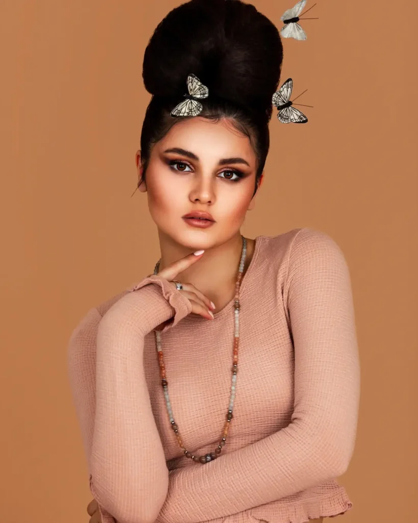 Mariana wearing a pink knit top and statement jewelry with butterflies in her updo
