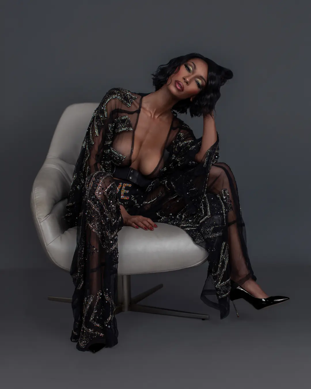 Jovona Logan seated in a black dress and heels against a grey backdrop