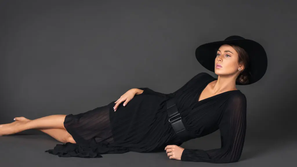Rebecca in a belted black dress and hat in a timeless editorial photograph