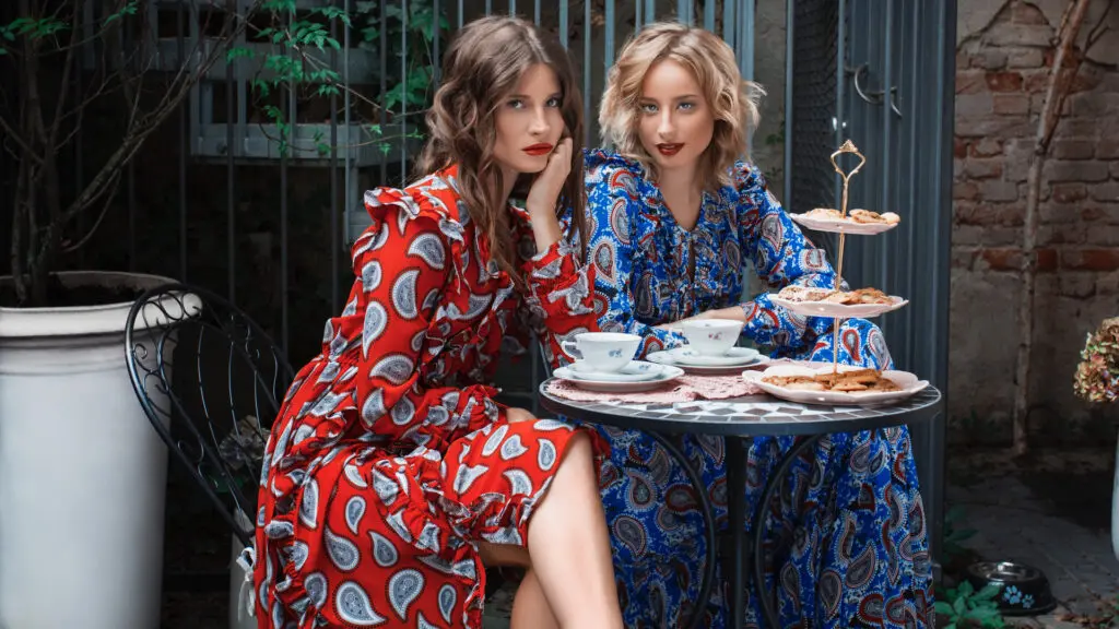Two women in colorful dresses having coffee in a Berlin garden