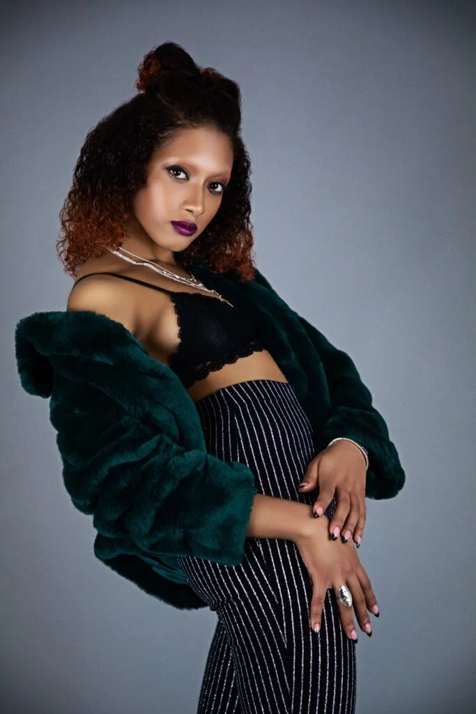 Model wearing a deep green jacket, black crop top and striped trousers