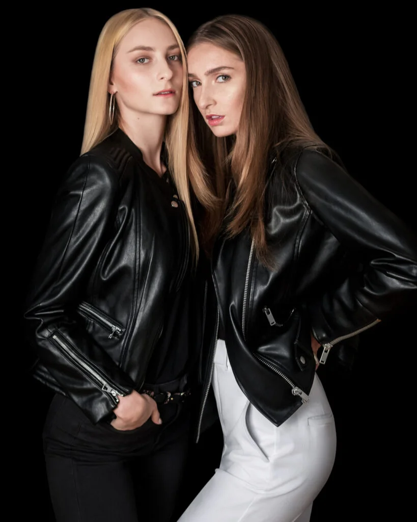 Two models wearing black leather jackets with black and white trousers