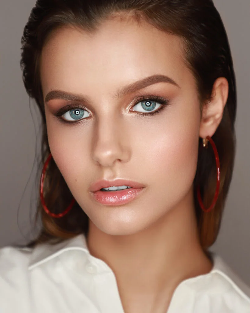 Woman with slicked-back hair, defined eye makeup and red hoop earrings